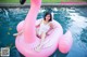 A woman sitting on an inflatable pink flamingo in a pool.