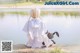 A girl sitting on the edge of a lake holding a stuffed animal.