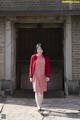 A woman in a red dress and red cardigan standing in front of a brick building.