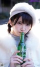 A woman in a white coat holding a green bottle of beer.